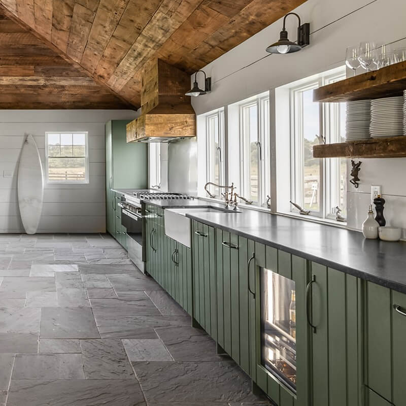 Open kitchen with green cabinetry, stone flooring, custom wood vent hood and a spacious dining table for entertaining.