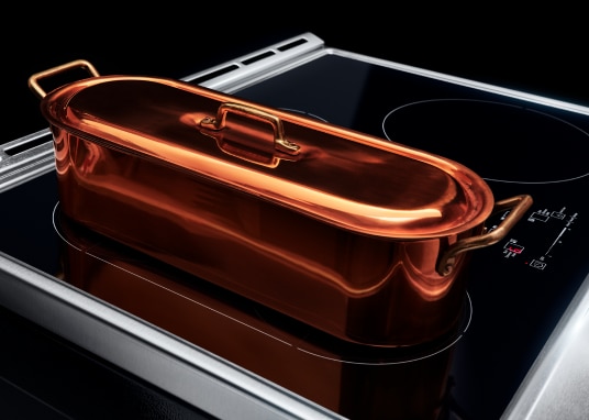 Specialty induction cookware placed on top of an induction cooktop with multiple cooking zones.