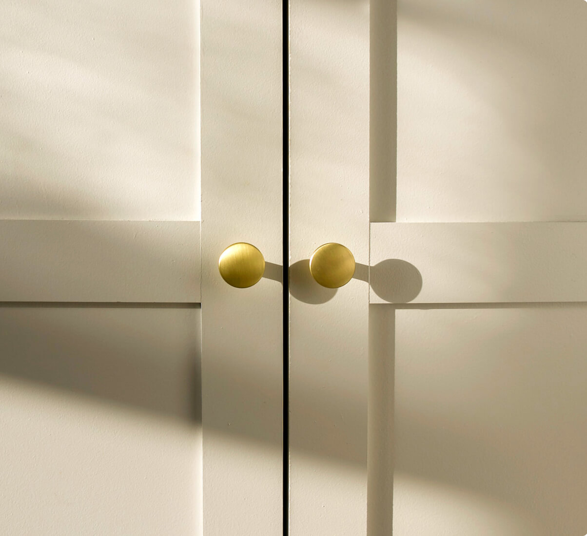 A close-up view of a white cabinet with two small, round brass knobs at the center. A close-up view of a white cabinet with two small, round brass knobs at the center.