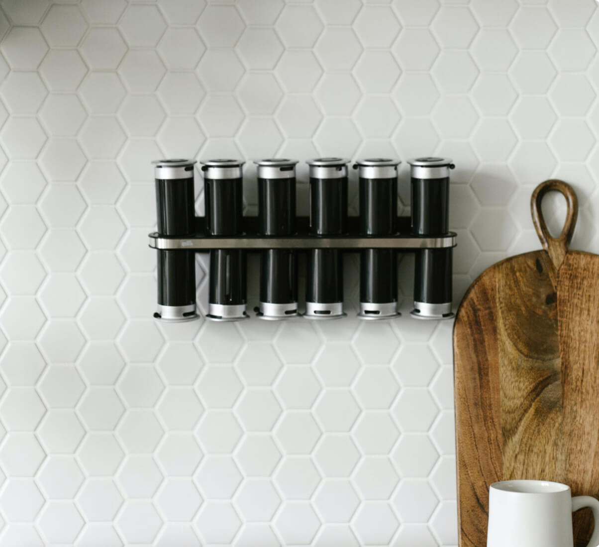 Hexagon-shaped white tile creates a honeycomb pattern backsplash, with a simple spice rack hanging on it. 