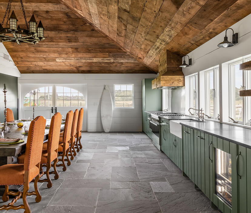 Open kitchen with green cabinetry, stone flooring, custom wood vent hood and a spacious dining table for entertaining