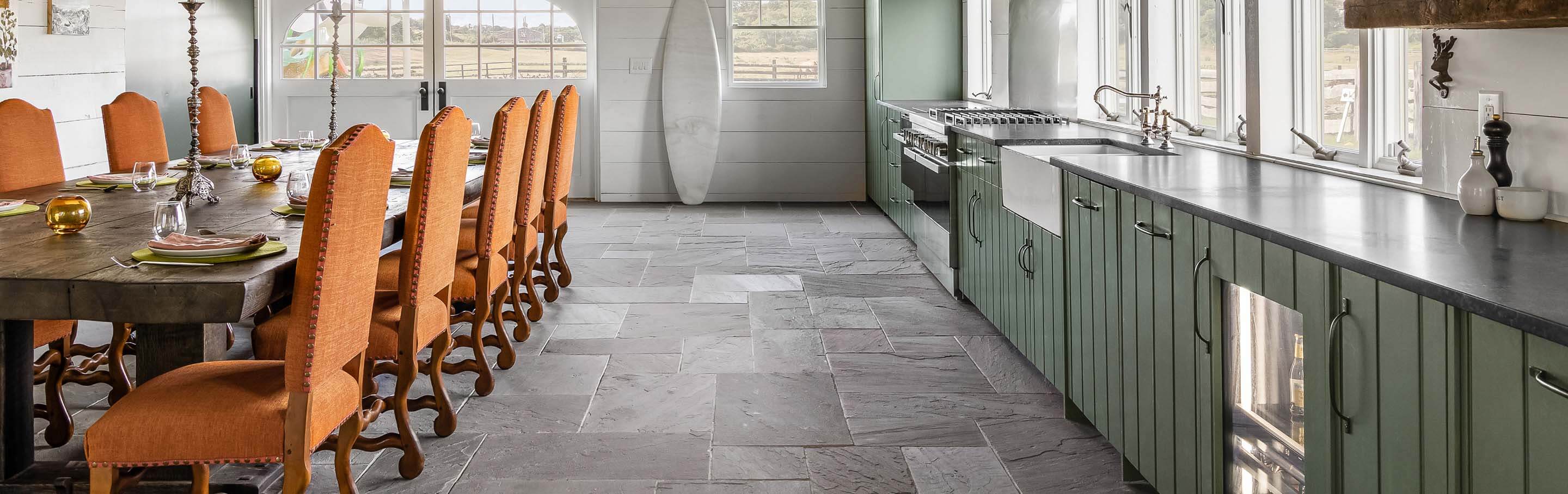 Open kitchen with green cabinetry, stone flooring, custom wood vent hood and a spacious dining table for entertaining