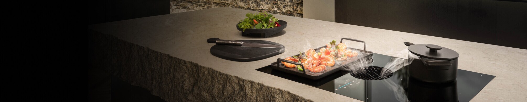 A JennAir® 36-Inch downdraft Induction Cooktop pulling steam away from a pan of cooking food.