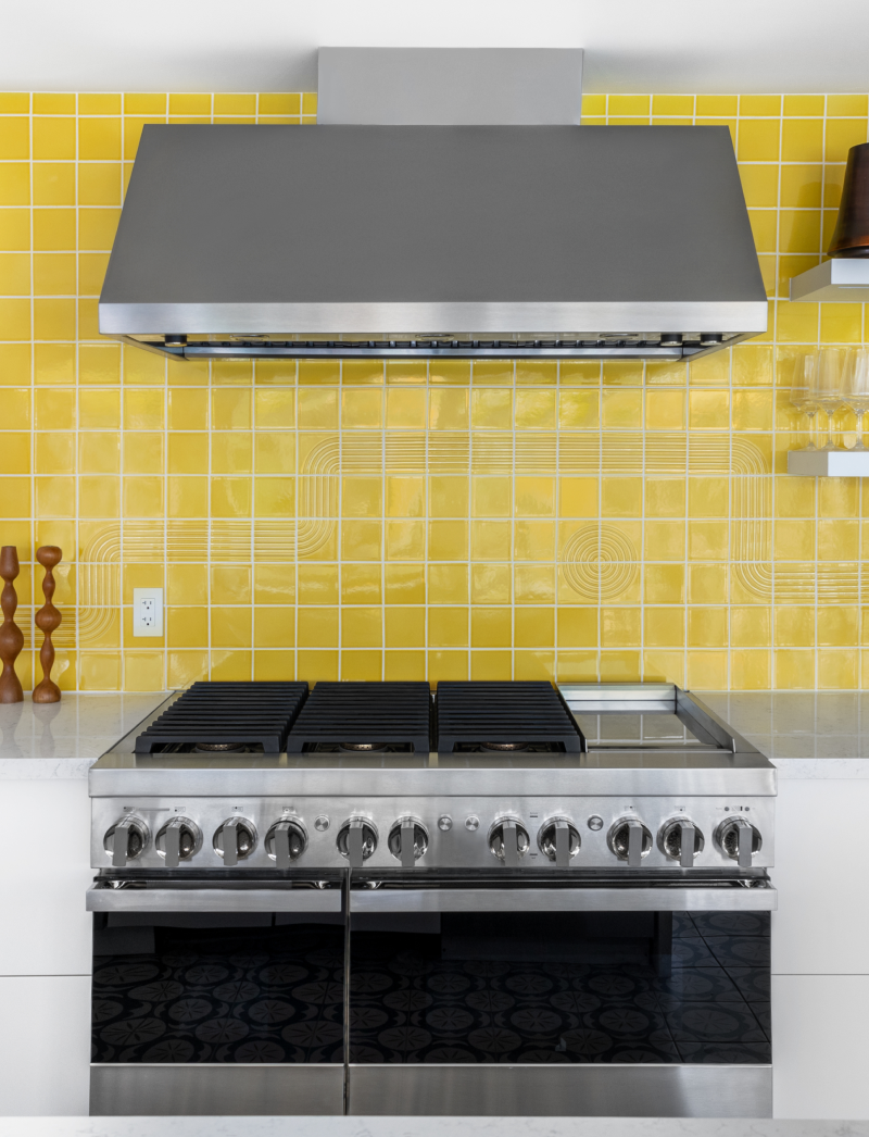 A JennAir® NOIR™ Professional Range and Commercial Hood in a kitchen with a yellow backsplash.