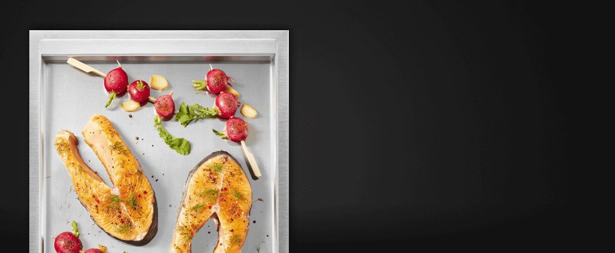 A close up of the griddle surface with salmon steaks and cherry tomato skewers on it.
