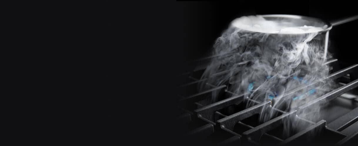 Steam from a pot being pulled down by downdraft ventilation on a gas cooktop.