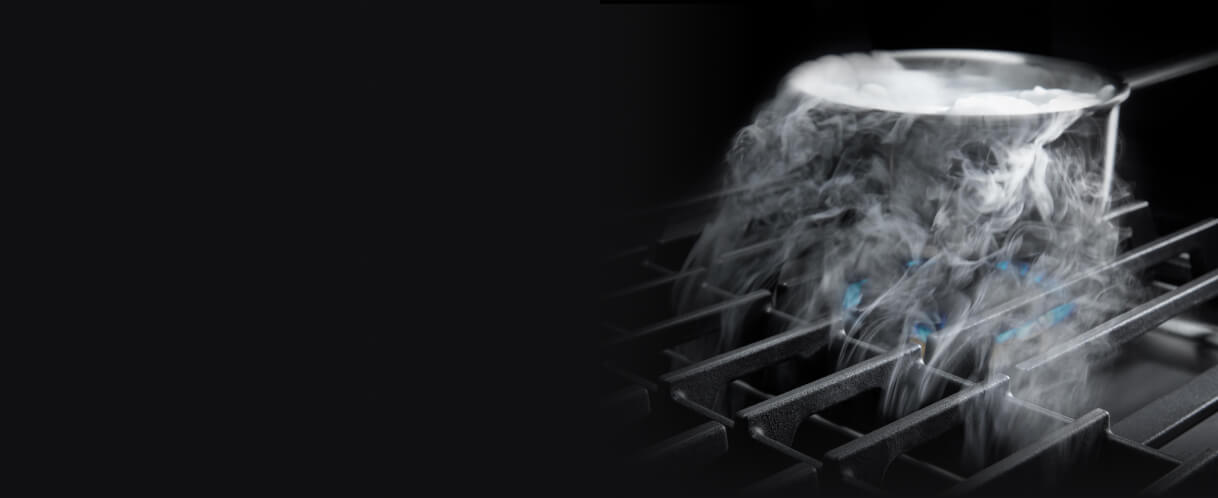 Steam from a pot being pulled down by downdraft ventilation on a gas cooktop.