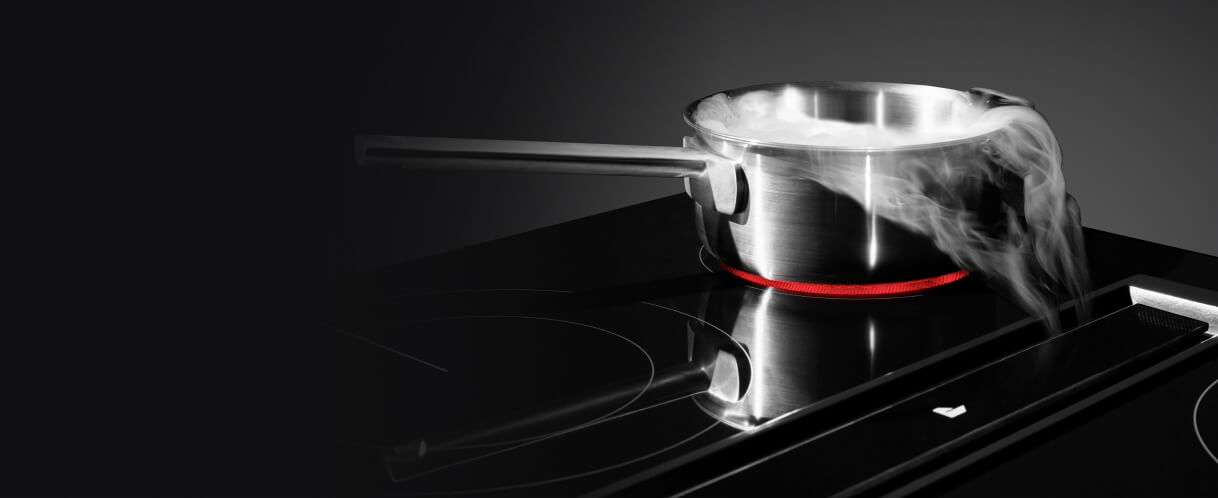 Steam from a pot being pulled down by downdraft ventilation on an electric radiant cooktop.