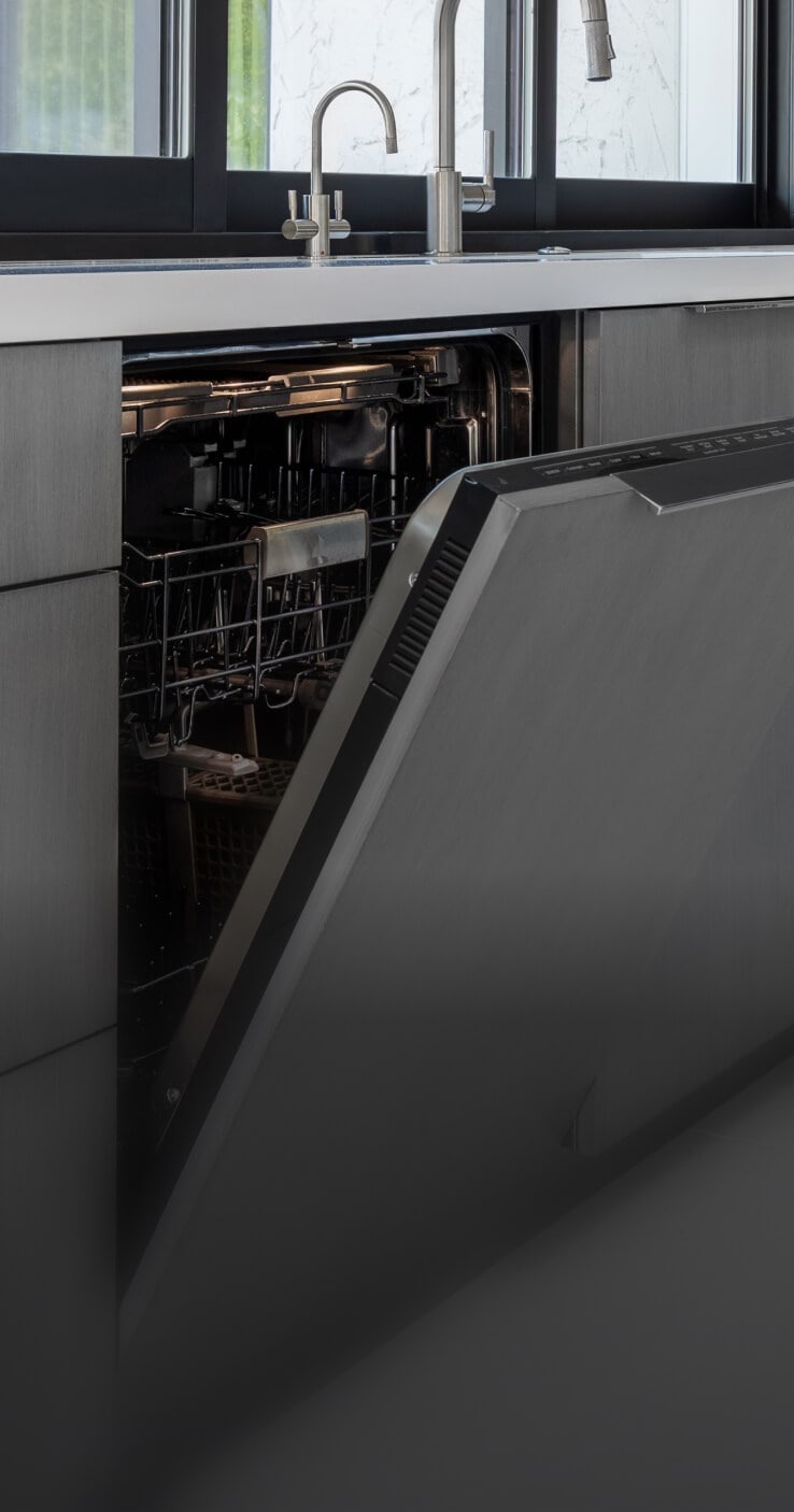 A JennAir® Panel-Ready Dishwasher with its door slightly ajar in a kitchen with gray cabinets.