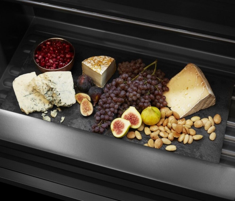 An open drawer filled with fruits and cheeses.