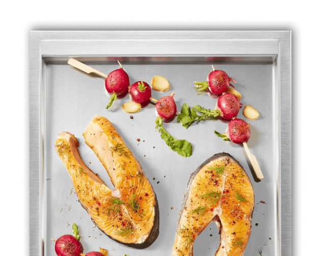 A close up of the griddle surface with salmon steaks and cherry tomato skewers on it.