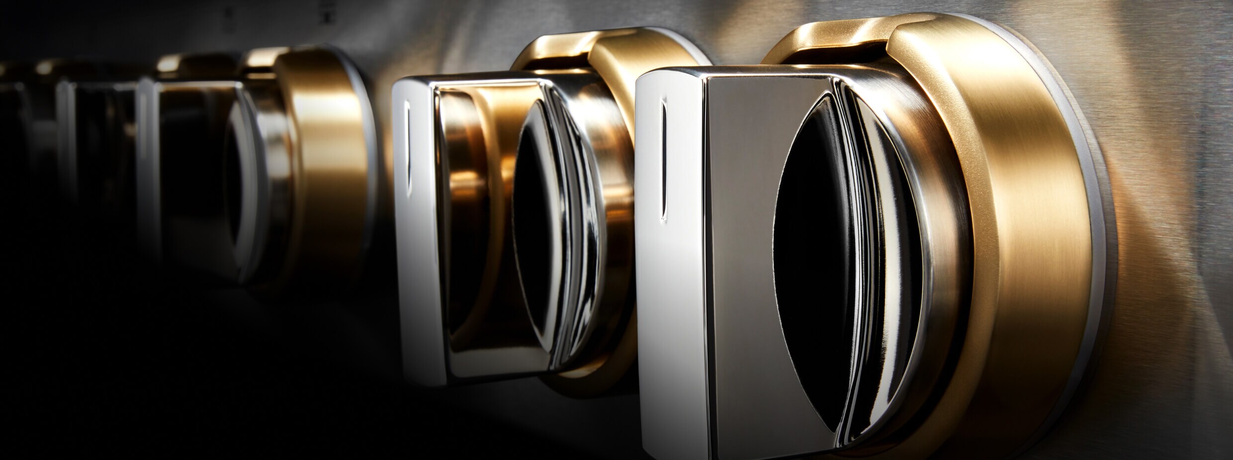 Closeup of the knobs of a JennAir® RISE™ Design Expression Rangetop, showing the brass details.