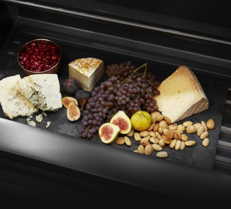 A drawer in a JennAir® refrigerator filled with cheeses and fruits.