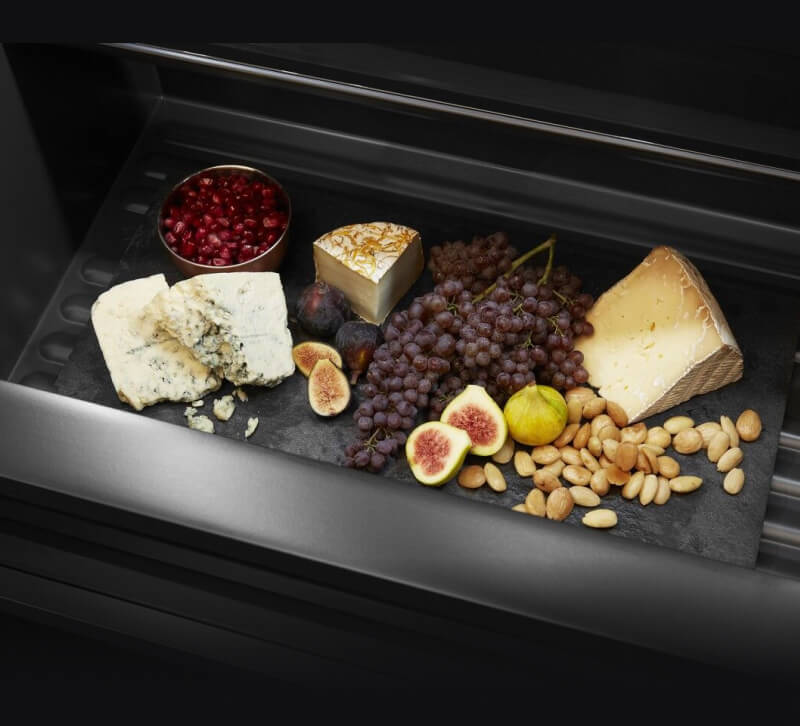 An open drawer filled with fruits and cheeses.
