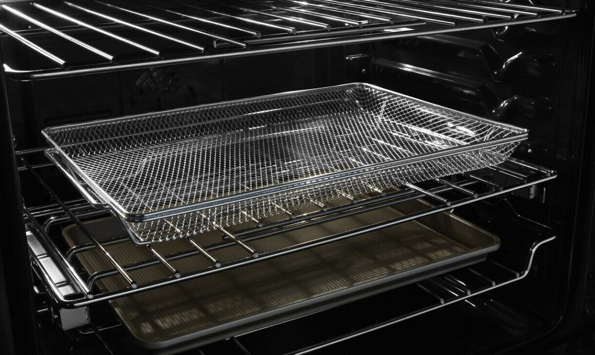 The illuminated interior of a slide-in range, with cookware on different racks.