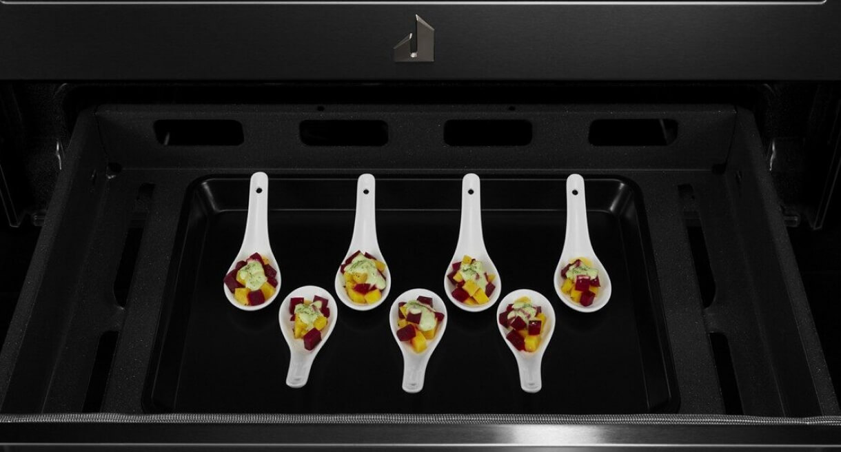 A set of serving spoons holding a portion of an appetizer in the compartment under the oven.