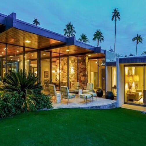 The exterior of a modern, stylish home looking into the living quarters through large glass windows. 