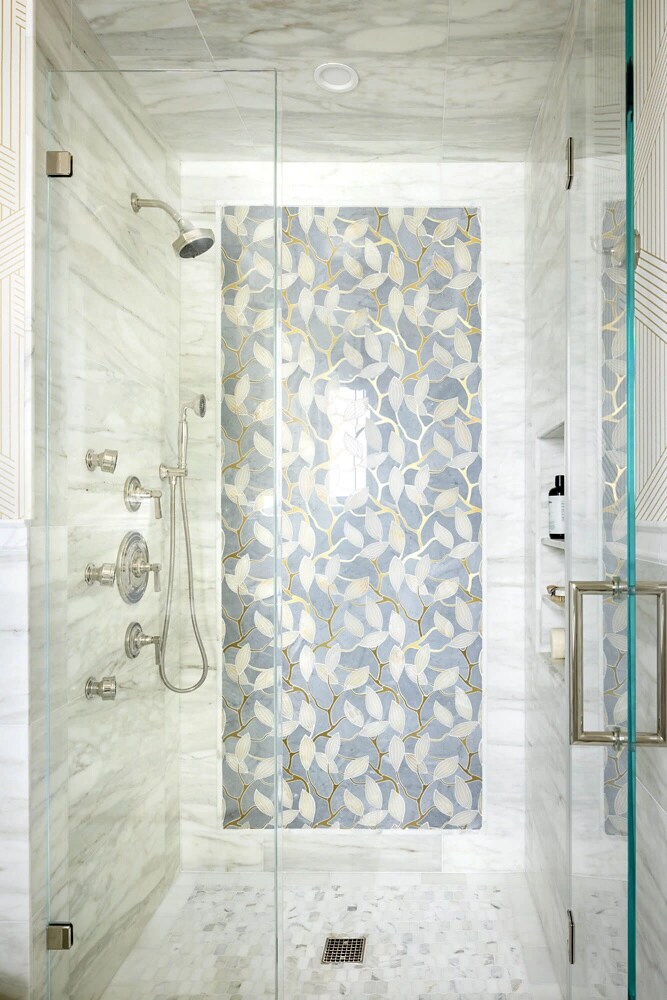 A white bathroom shower in marble with an accent tile wall.