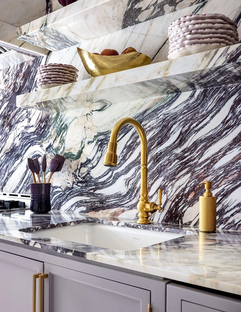 A close up on a brass faucet and a white porcelain sink in a marble kitchen.