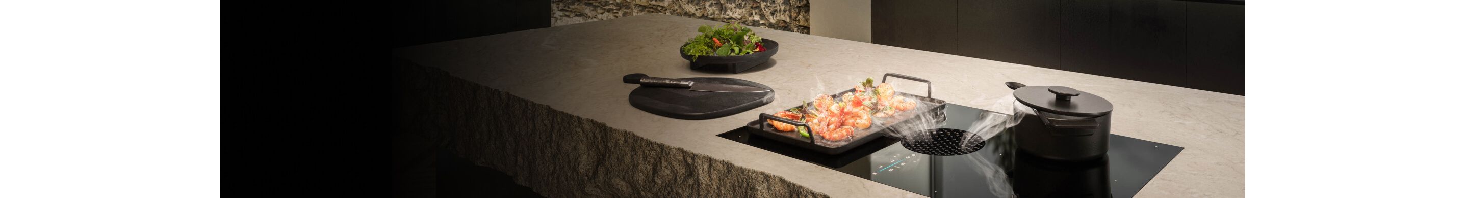 A JennAir® 36-Inch downdraft Induction Cooktop pulling steam away from a pan of cooking food.