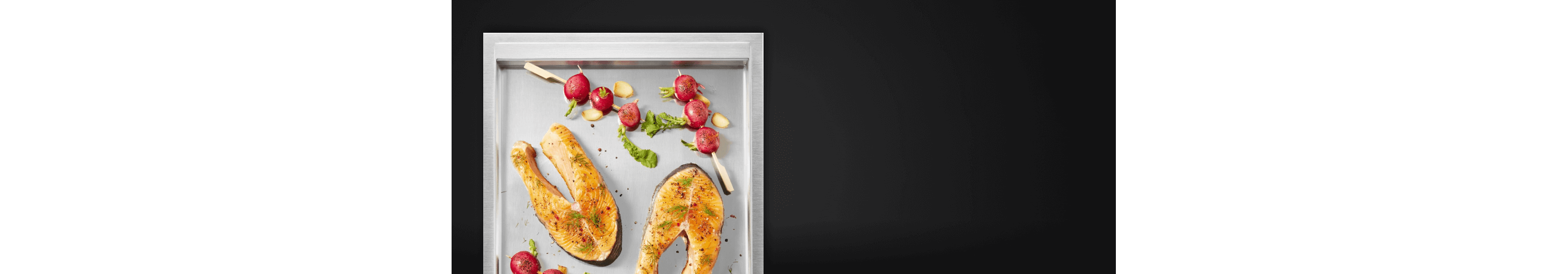 A close up of the griddle surface with salmon steaks and cherry tomato skewers on it.