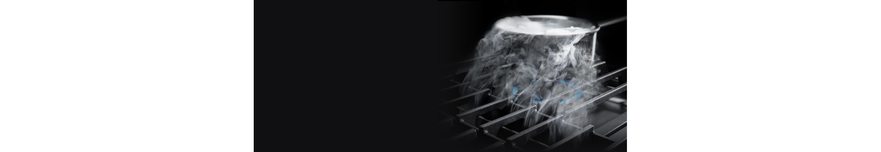 Steam from a pot being pulled down by downdraft ventilation on a gas cooktop.