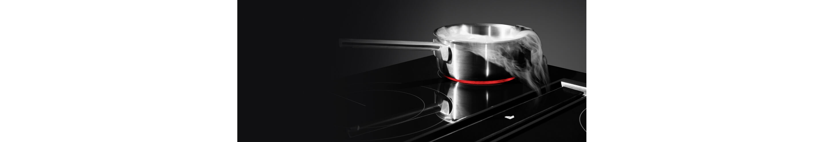 Steam from a pot being pulled down by downdraft ventilation on an electric radiant cooktop.
