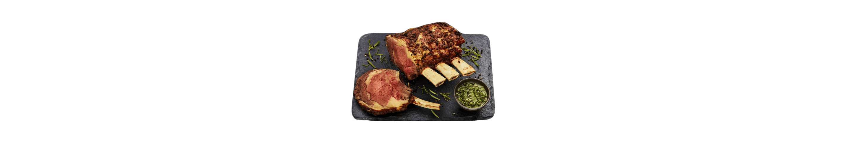 A cooked medium-rare crown roast on a slate with chimichurri sauce.