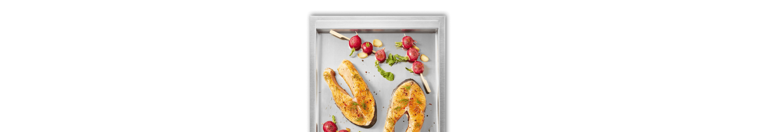 A close up of the griddle surface with salmon steaks and cherry tomato skewers on it.