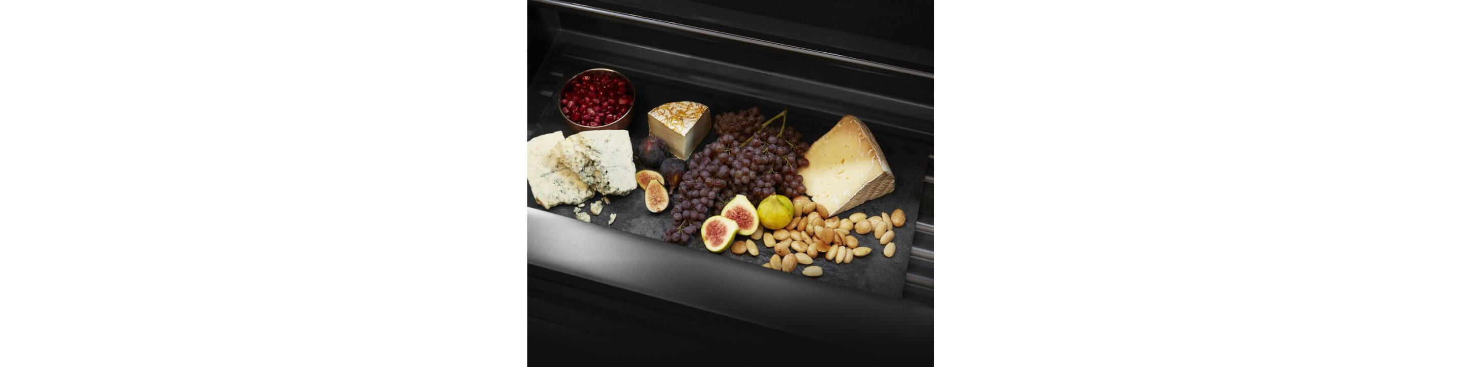 A drawer in a JennAir® refrigerator filled with cheeses and fruits.