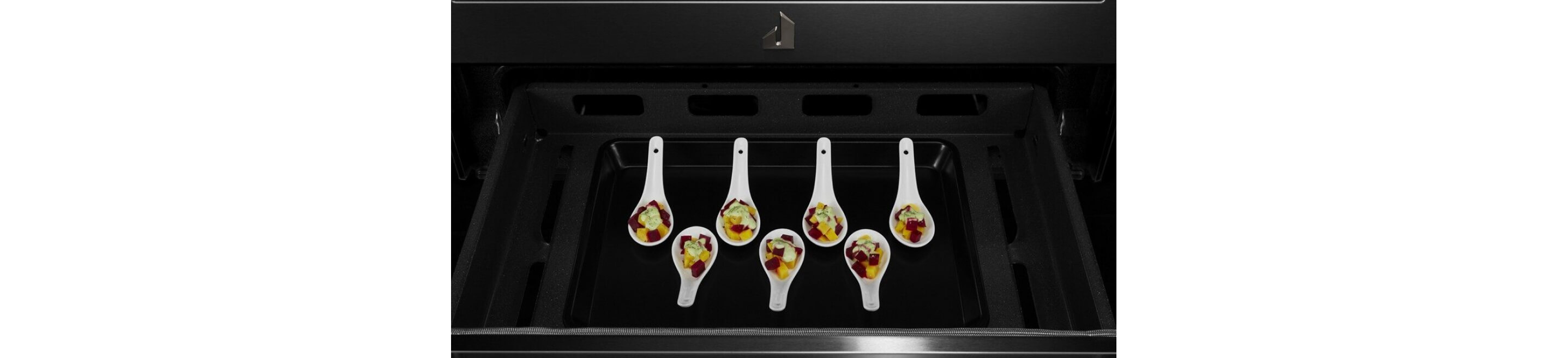A set of serving spoons holding a portion of an appetizer in the compartment under the oven.