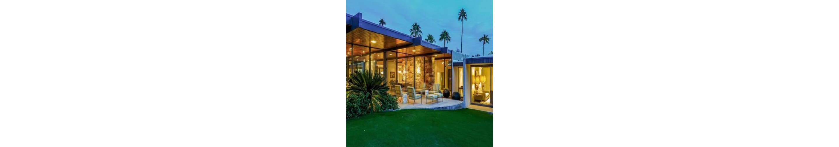 The exterior of a modern, stylish home looking into the living quarters through large glass windows. 