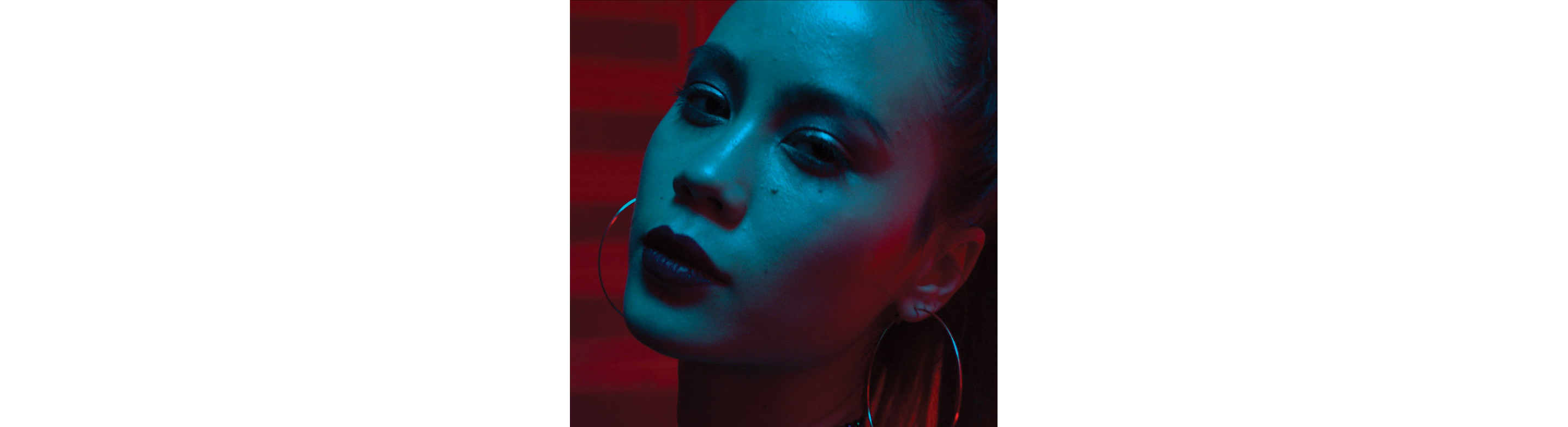 A defiant woman looking into the camera, with blue lights on her face and red lights illuminating the background. 