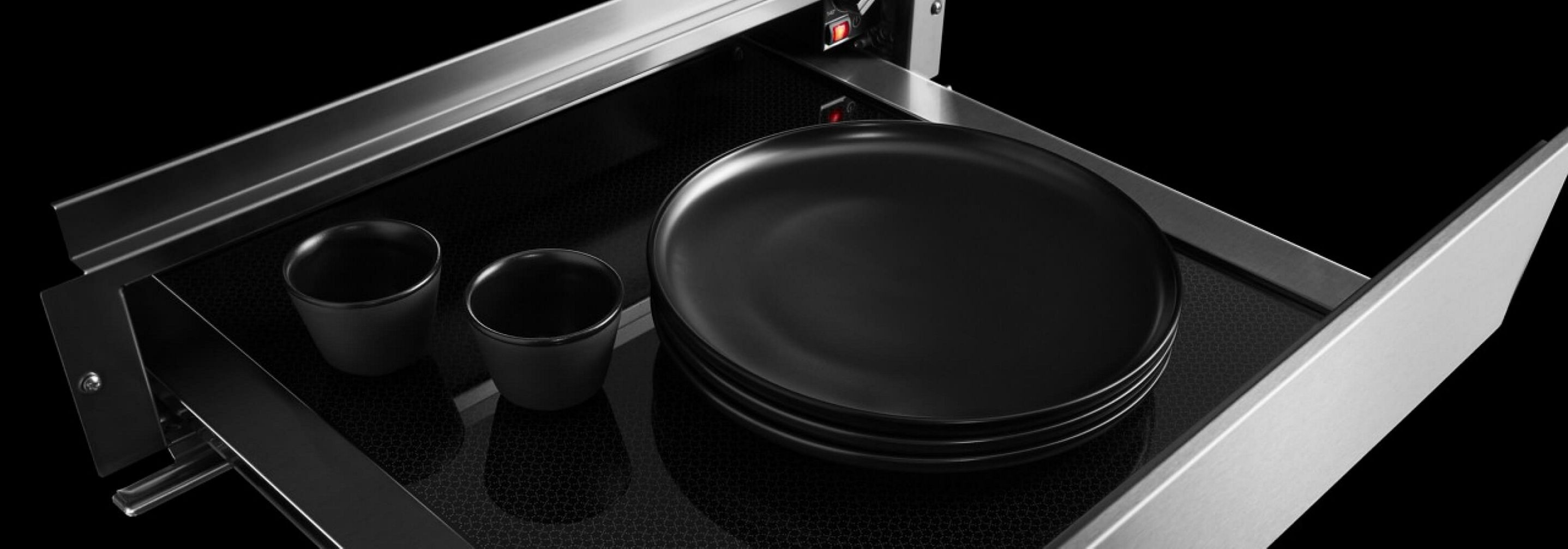 An open JennAir® 24-inch warming drawer with plates and mugs inside.