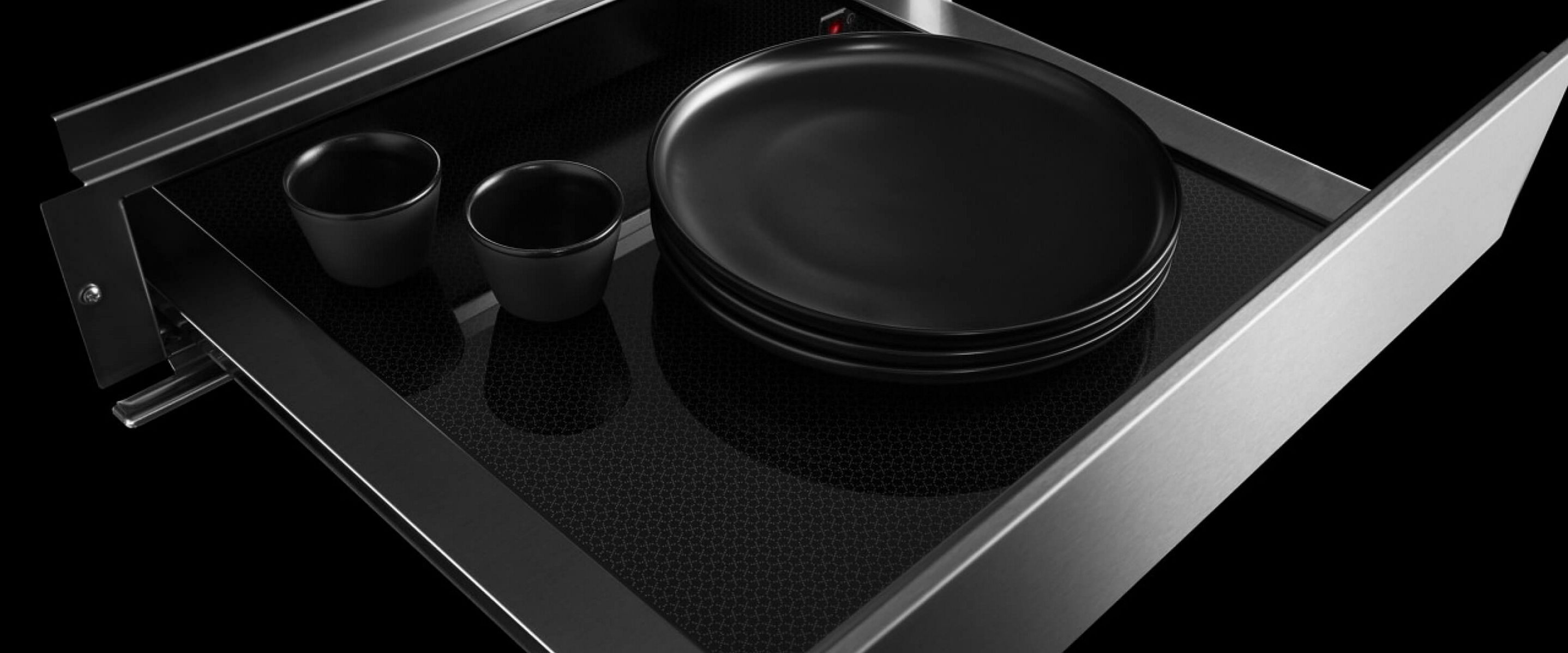 An open JennAir® 24-inch warming drawer with plates and mugs inside.